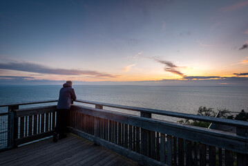 Obraz premium Man standing alone on view point by lake looking at sunset
