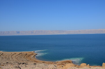 Panoramic view of the beautiful, clear blue Dead Sea shimmering and shining on a bright sunny day in Jordan and the dry land around it.