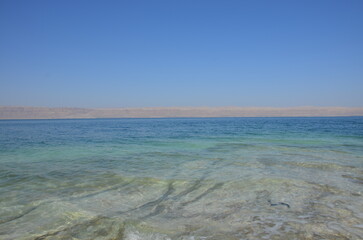 Panoramic view of the beautiful, clear blue Dead Sea shimmering and shining on a bright sunny day in Jordan and the dry land around it.