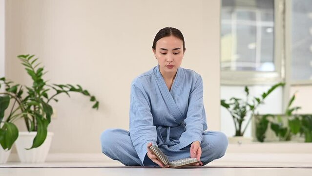Asian woman opens wooden boards Sadhu with nails while sitting on yoga mat.
