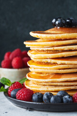 Delicious pancakes, with fresh blueberries, raspberry and maple syrup or honey on a dark background