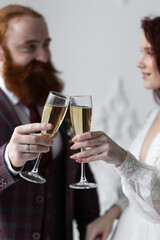 Beautiful red-hair bride in a white wedding dress and bouquet of flowers wearing pearls and a handsome groom with a red beard in a suit. Young loving couple. Drinking champagne
