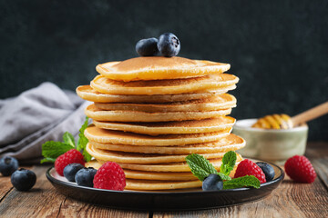 Delicious pancakes, with fresh blueberries, raspberry and maple syrup or honey on a dark background
