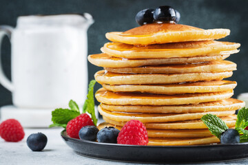 Delicious pancakes, with fresh blueberries, raspberry and maple syrup or honey on a dark background