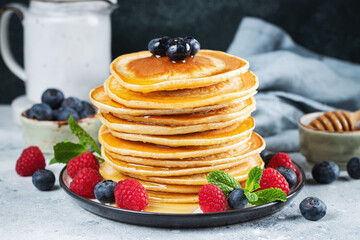 Delicious pancakes, with fresh blueberries, raspberry and maple syrup or honey on a dark background