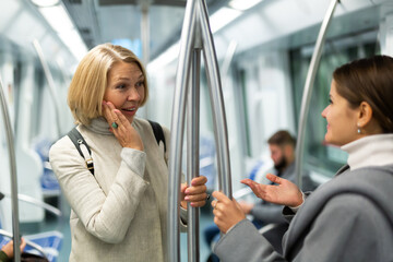 Portrait of mature woman talking friendly with her fellow traveler in modern subway car..