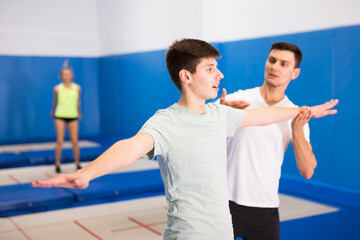 Obraz na płótnie Canvas Male instructor helping teenage boy warming up before trampoline training in fitness center