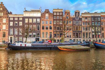Cityscape on a sunny winter day - view of the houses and the city canal with boats in the historic center of Amsterdam, The Netherlands