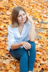 Portrait of a blonde caucasian girl sitting on falling yellow leaves and smiling