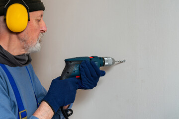 Man drilling a hole in the wall with an electric drill.