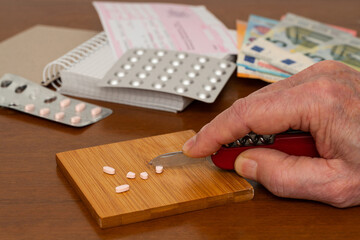 Human hand divides medical pills with a knife on a wooden table. Close up.
