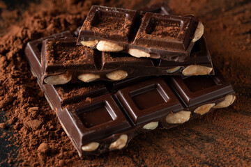 Dark and milk chocolate with nuts on a dark background sprinkled with cocoa powder.