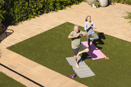 Happy senior diverse couple doing yoga and meditating in garden