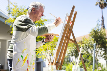 Happy senior caucasian man painting on easel in garden
