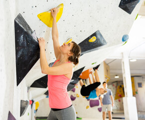 Young female alpinist practicing indoor rock-climbing on a artificial boulder without the safety...