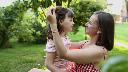 Family day, mother's day. Smiling young mom and little child daughter looking and touching each other spending time together on the backyard lawn. Idyllic family having fun outdoors on summer holiday.