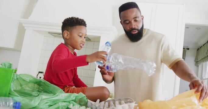 Happy african american father and son sorting waste in kitchen, in slow motion
