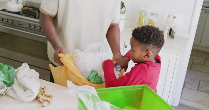 Happy african american father and son sorting waste in kitchen, in slow motion