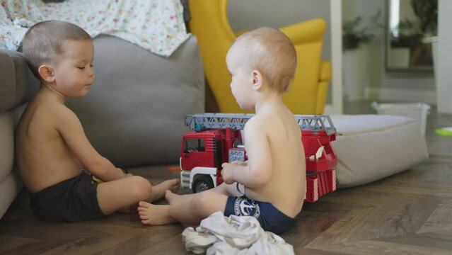 two little boys brother siblings playing toy fire engine red fire truck rescue team on floor at home daytime. baby boys kids imagine being firefighters play together activity games indoors developing 