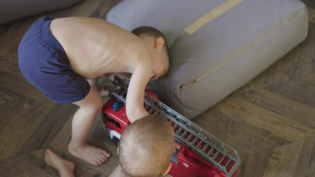 two little boys brother siblings playing toy fire engine red fire truck rescue team on floor at home daytime. baby boys kids imagine being firefighters play together activity games indoors developing 