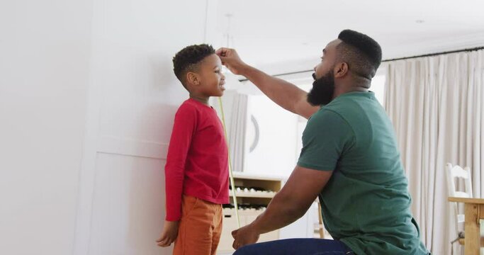 Happy african american father and son measuring height, in slow motion