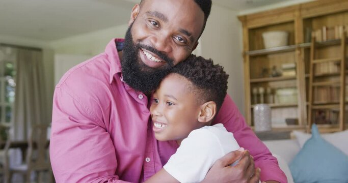 Portrait of happy african american father and son sitting on sofa and embracing, in slow motion