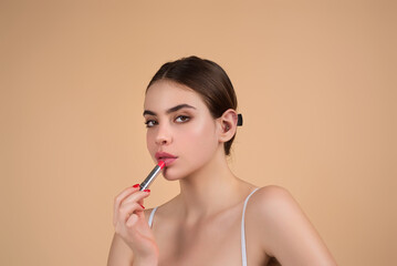 Studio portrait of beautiful woman with red lipstick. Beautiful young woman applying lipstick on her lips, isolated on studio background.