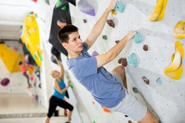 Male alpinist practicing indoor rock-climbing on artificial boulder without safety belts