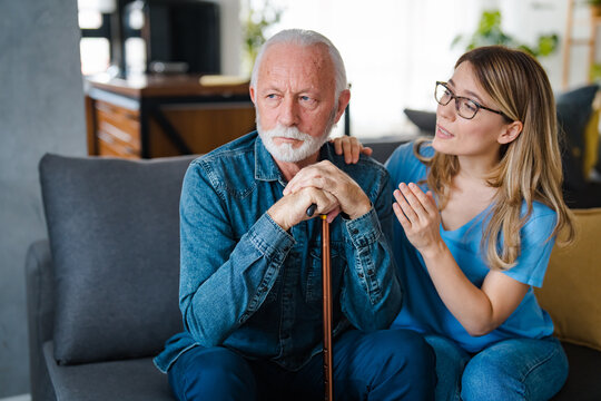 Community Nurse Visits Senior Man Suffering With Depression. A Woman Carer Concerned About An Elderly Man Looking Depressed. Desperate Sad Pensioner Living In Residential Home