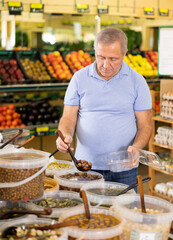 in large self-service supermarket, man buyer puts large olives in container