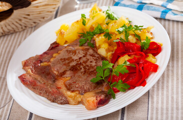 Fototapeta premium Juicy veal steak with vegetable garnish of fried potatoes, pickled bell pepper and fresh greens