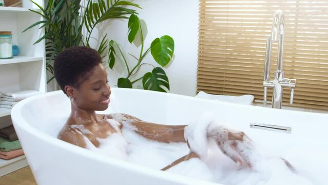 Smiling young woman enjoy foam bath washes skin with soap. Self care relax spa time and beauty body