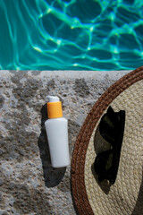white mock up sunscreen bottle at the pool with sunglasses and summer hat
