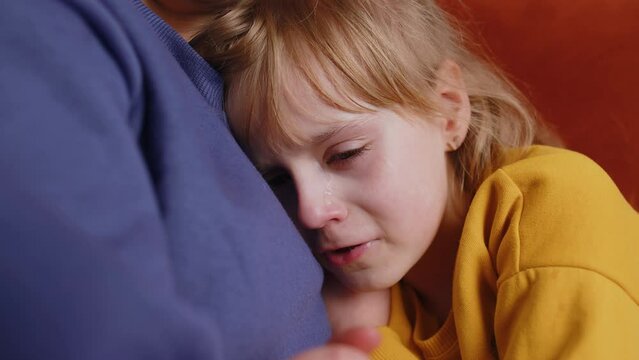 Close-up portrait of upset child little girl kid crying with tears flowing down on her cheek, toddler lies on mother at home. Mom hugs, embrace, takes pity on her daughter. Quarrel, bullying at school