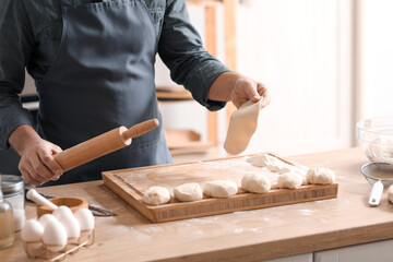 Male baker rolling out dough at table in kitchen, closeup