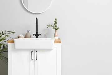 Ceramic sink with bath accessories, reed diffuser and eucalyptus in vase near light wall