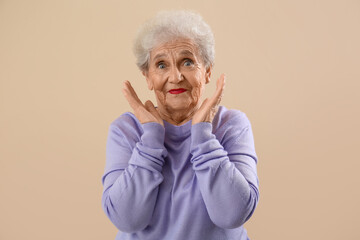 Surprised senior woman in lilac sweater on beige background