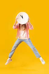 Little girl with wall clock jumping on yellow background