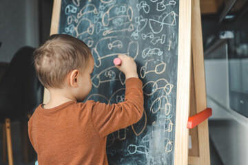 A small child draws a chalk on an easel