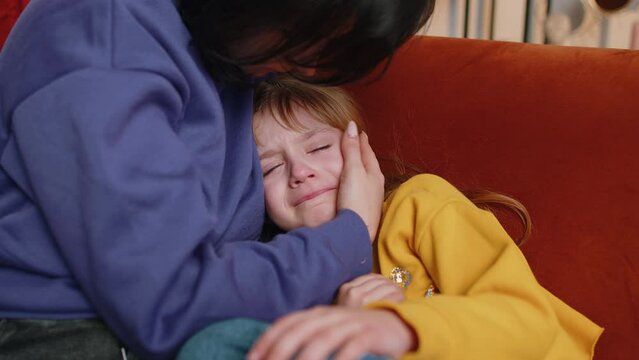 Offended sad girl kid is crying and lying on mother at home. Violence against children in family. Quarrel, bullying at school. Child toddler abuse. Mom hugs, embrace, takes pity on her daughter