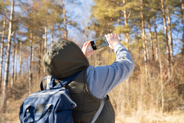 Back view photo of a female hiker with a backpack taking a photo with her mobile phone of the beautiful nature around her.