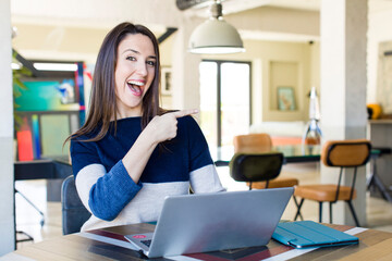 young pretty woman looking excited and surprised pointing to the side. telecommuting concept
