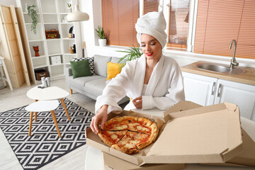 Young woman in bathrobe with tasty pizza sitting at home