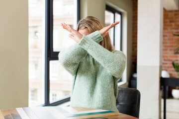 young pretty woman covering face with hand and putting other hand up front to stop camera, refusing...