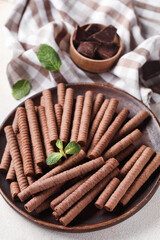 Plate with delicious chocolate wafer rolls on white background