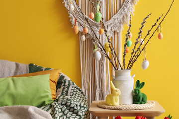 Vase with willow branches, Easter eggs and rabbits on table in living room