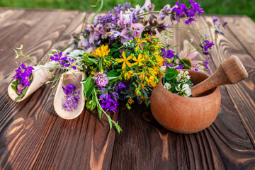 Fototapeta na wymiar Summer medicinal herbs - St. John's wort, chamomile, clover near wooden mortar. Preparation of medicines from natural plants by herbalists