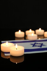 Obraz na płótnie Canvas Burning candles with flag of Israel on dark background, closeup. International Holocaust Remembrance Day