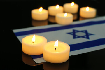 Burning candles with flag of Israel on dark background, closeup. International Holocaust Remembrance Day