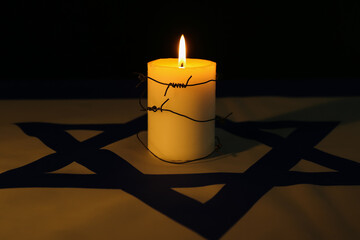 Burning candle with barbed wire on flag of Israel against dark background. International Holocaust...